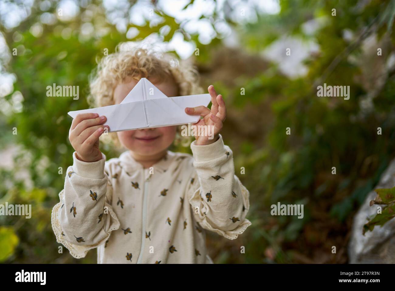 Ragazza felice che tiene la barca di carta in faccia davanti all'albero Foto Stock