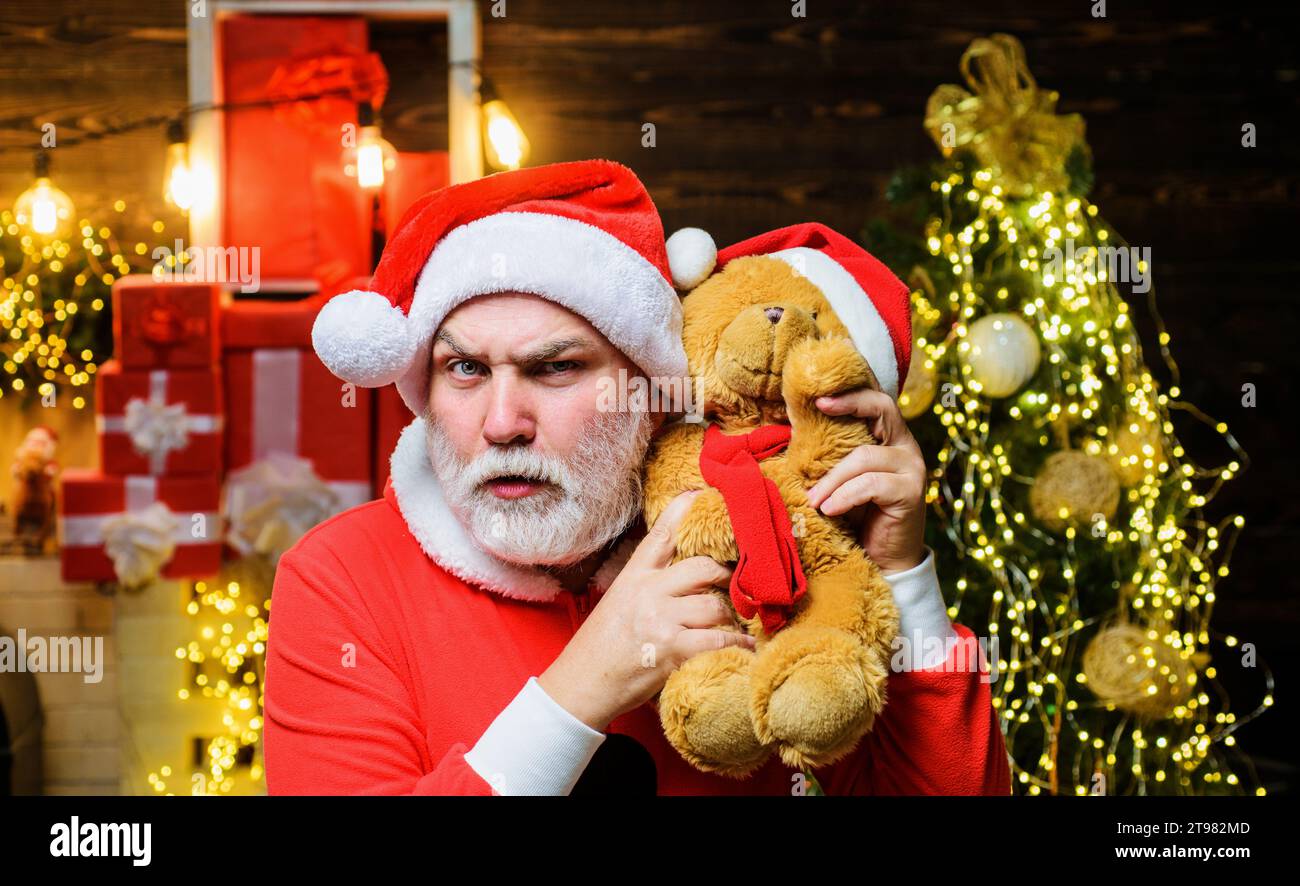 Festeggiamenti natalizi. Un uomo dalla barba seria in costume di Babbo Natale con orsacchiotto. Regalo di Natale e regalo. Babbo Natale con peluche giocattolo in peluche Foto Stock