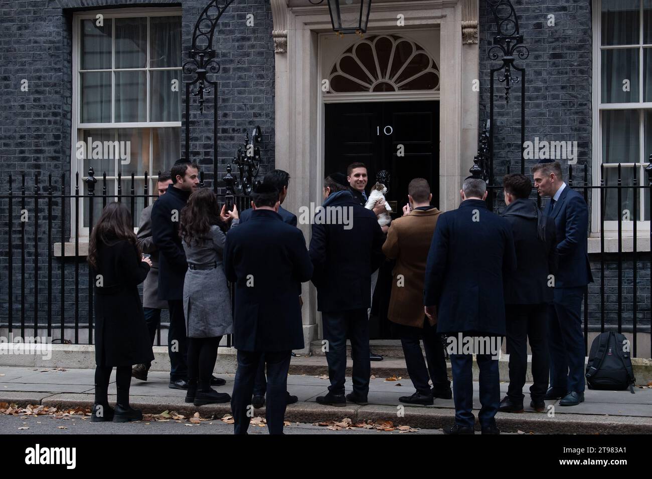 Londra, Regno Unito. 22 novembre 2023. Un gruppo di visitatori ebrei al numero 10. Downing Street, era felice di avere la loro fotografia scattata fuori dalla famosa porta d'ingresso e soprattutto così, come il capo mouser, il gatto numero 10 di Downing Street, Larry, si unì a loro per una foto. Credito: Maureen McLean/Alamy Live News Foto Stock