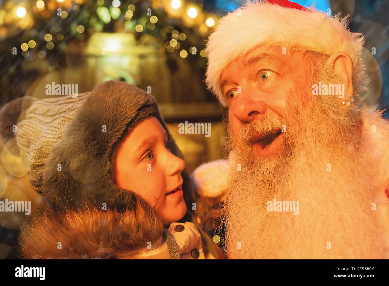 Un bambino in soggezione con Babbo Natale in un mercatino di Natale, circondato da luci festive Foto Stock