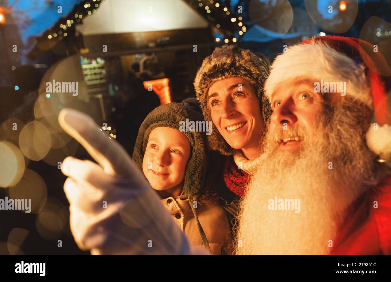 Famiglia con bambino e Babbo Natale al mercatino di Natale, luci bokeh e meraviglia nei loro occhi Foto Stock