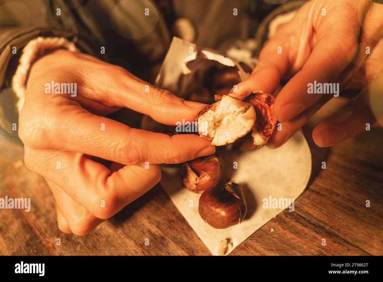 Le mani che pelano una castagna arrostita calda in un mercatino di Natale, con un caldo bagliore Foto Stock