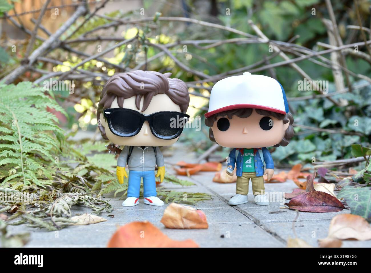 Funko Pop action figure di Steve e Dustin della popolare serie televisiva horror Stranger Things. Strada abbandonata, foresta autunnale, foglie, rami di alberi. Foto Stock