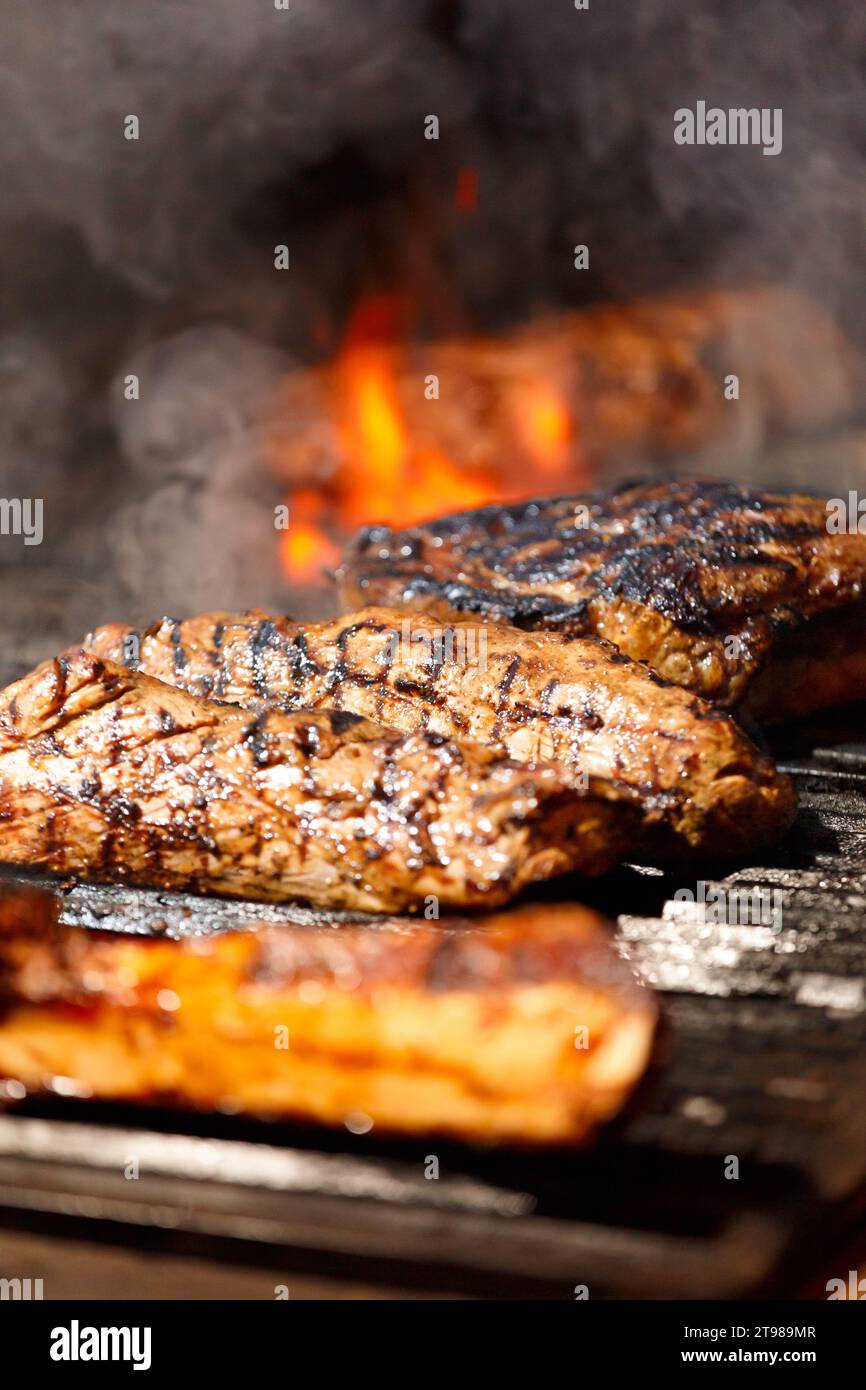 Appetitose bistecche di tomahawk, ribeye e controfiletto disposti su un barbecue con una fiamma incandescente durante la cottura alla griglia. Carne alla griglia in un ristorante. Foto Stock