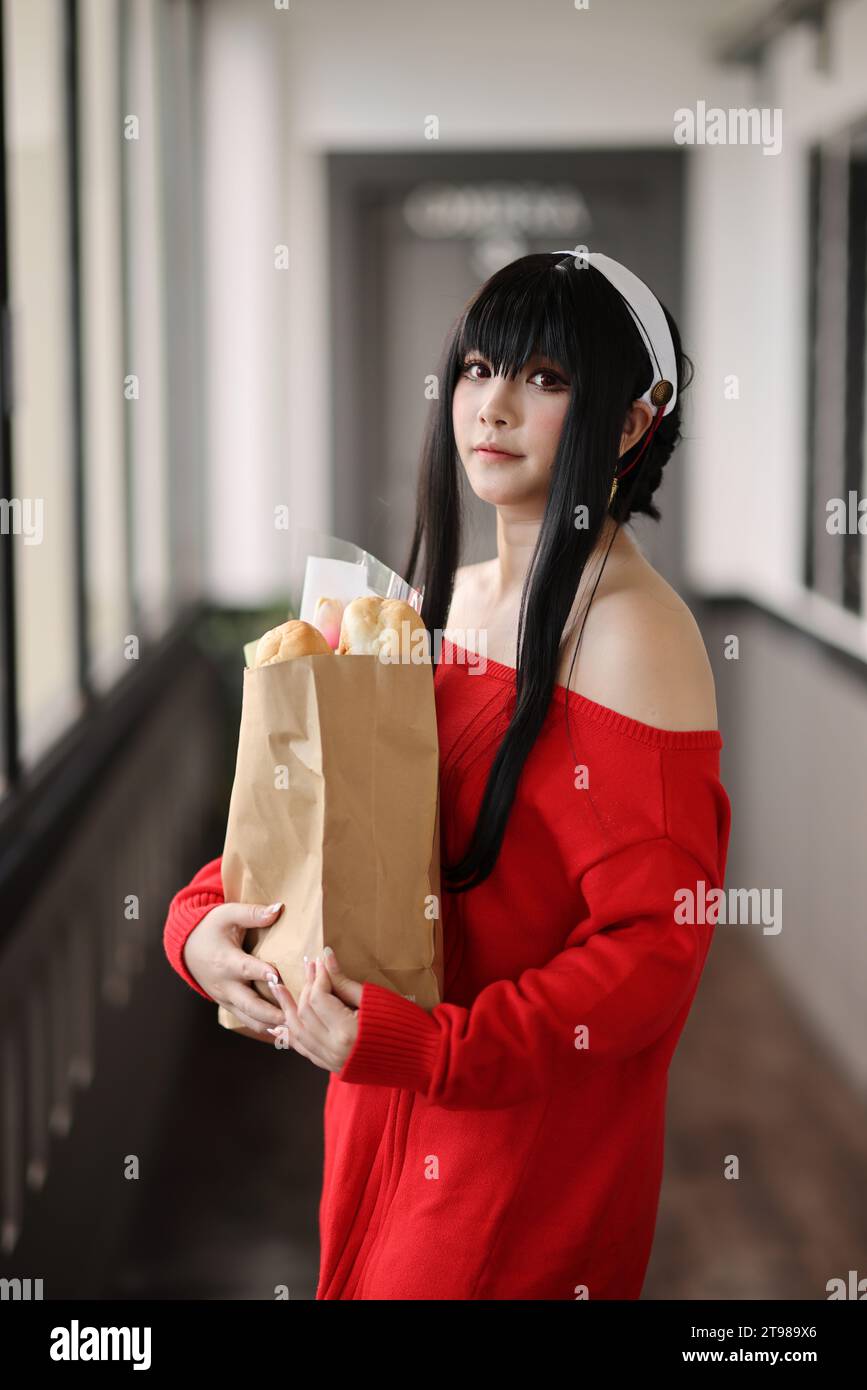 Ritratto di una bella giovane donna Cosplay con maglione rosso con pane nella borsa della spesa nel corridoio Foto Stock