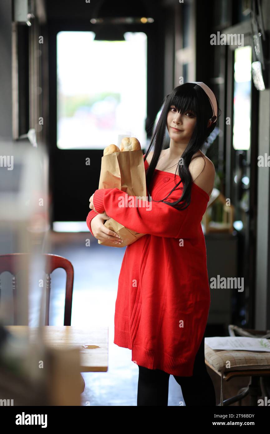 Ritratto di una bella giovane donna Cosplay con maglione rosso con pane nella borsa della spesa nel corridoio Foto Stock