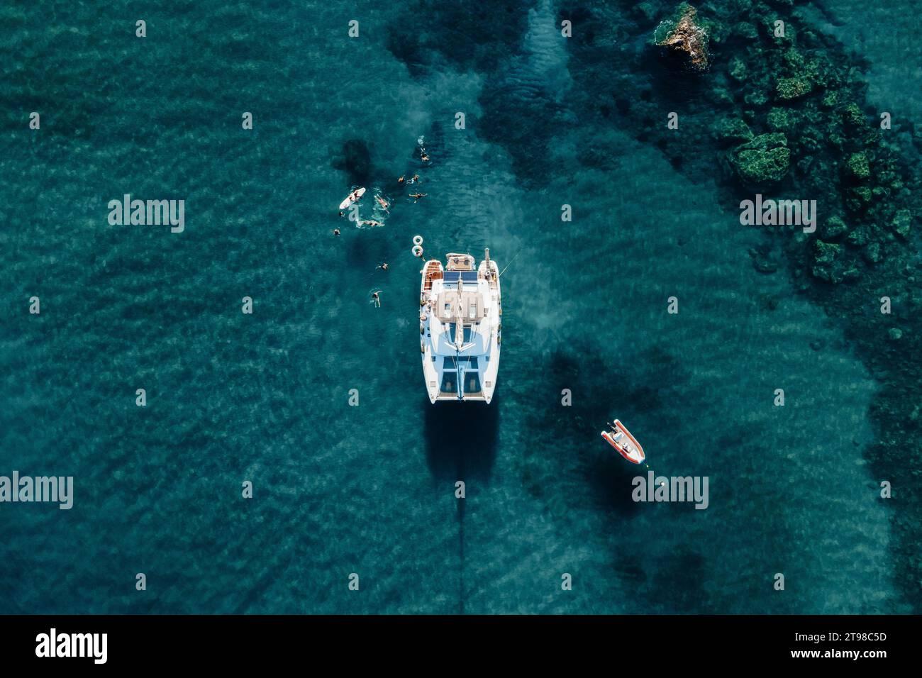Vista droni del catamarano ancorato nel mare blu con gente che nuota in estate. Sfondo del viaggio. Vacanze in crociera. Foto Stock
