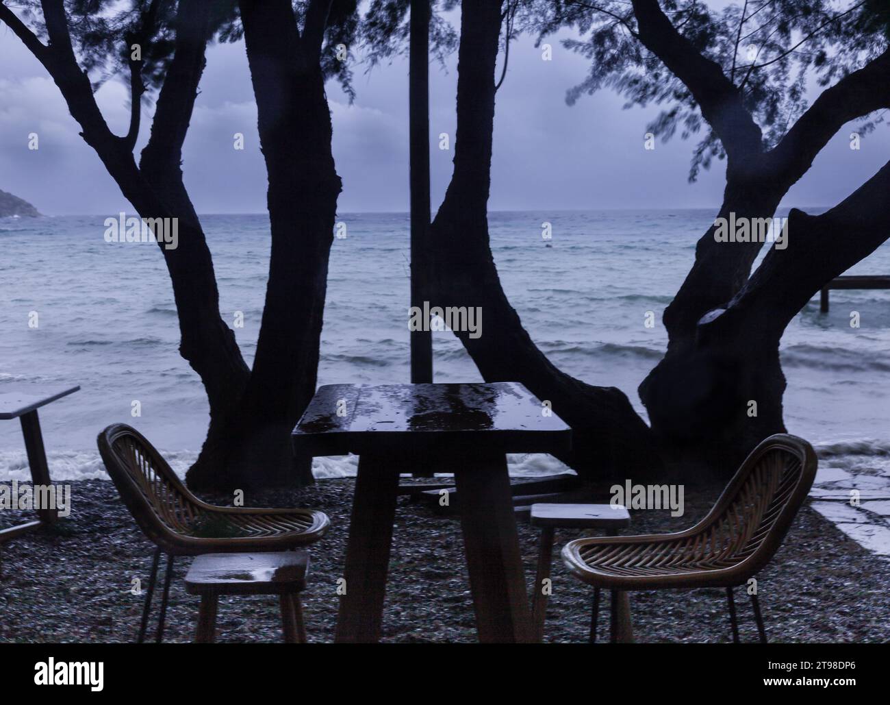 Paesaggio invernale in una città di mare. Sedie e tavoli vuoti in una giornata di pioggia. Una vista deprimente. Foto Stock