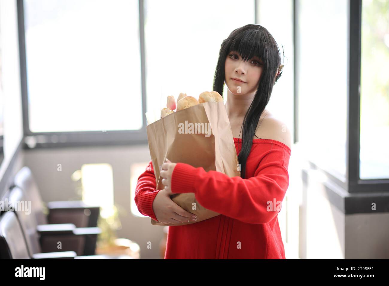 Ritratto di una bella giovane donna Cosplay con maglione rosso con pane nella borsa della spesa nel corridoio Foto Stock