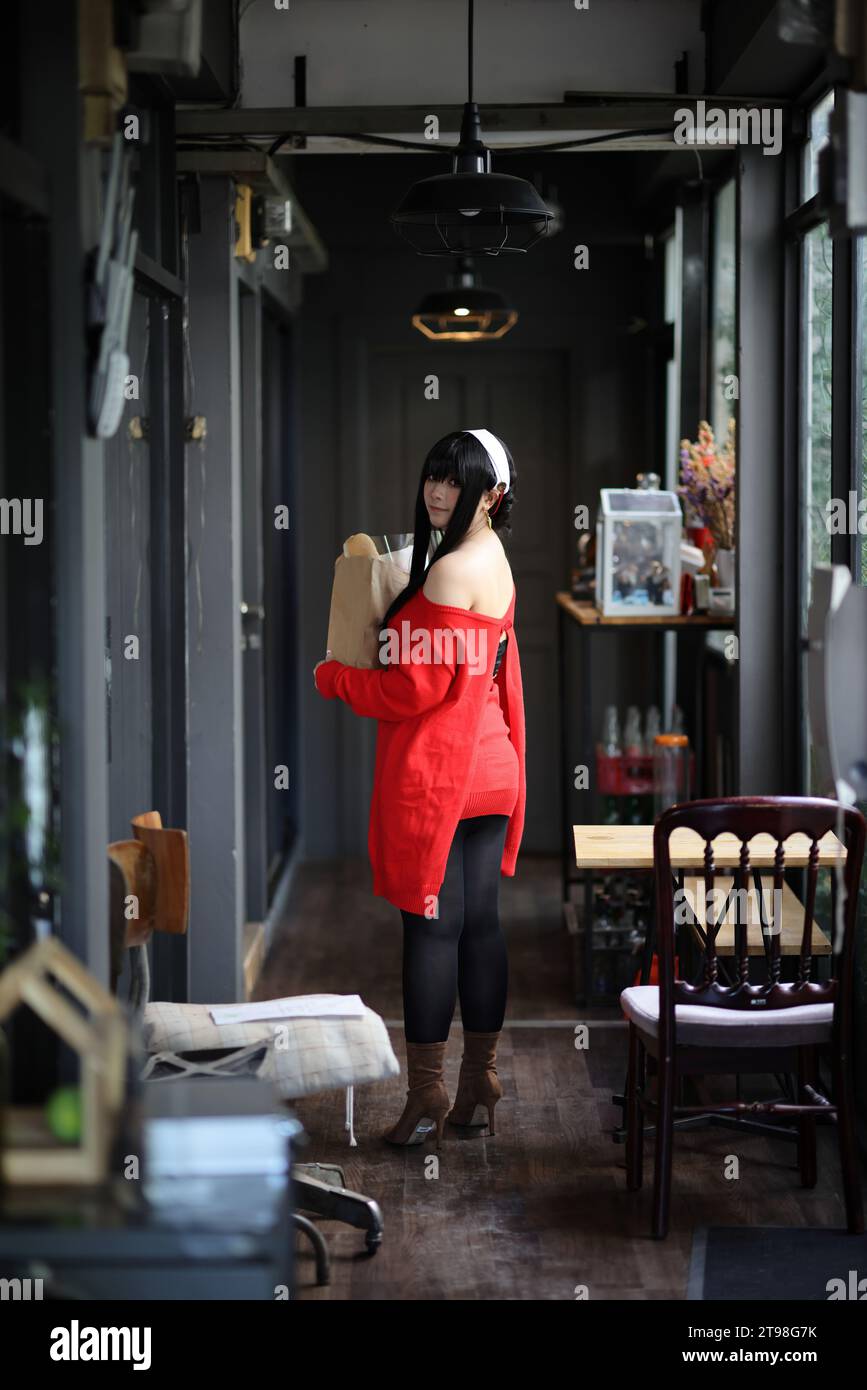 Ritratto di una bella giovane donna Cosplay con maglione rosso con pane nella borsa della spesa nel corridoio Foto Stock