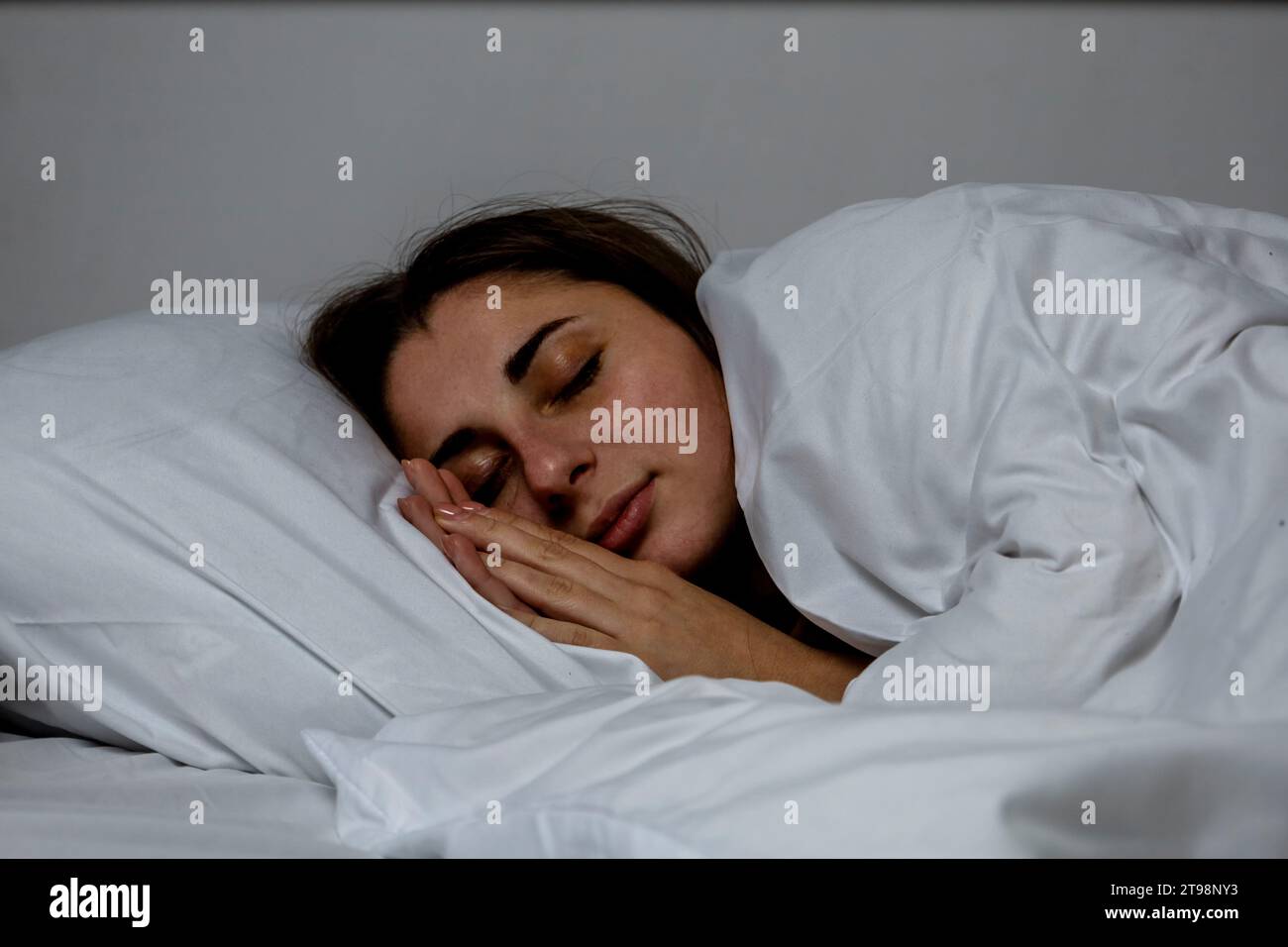 La ragazza sta dormendo in un letto con un lenzuolo bianco Foto Stock