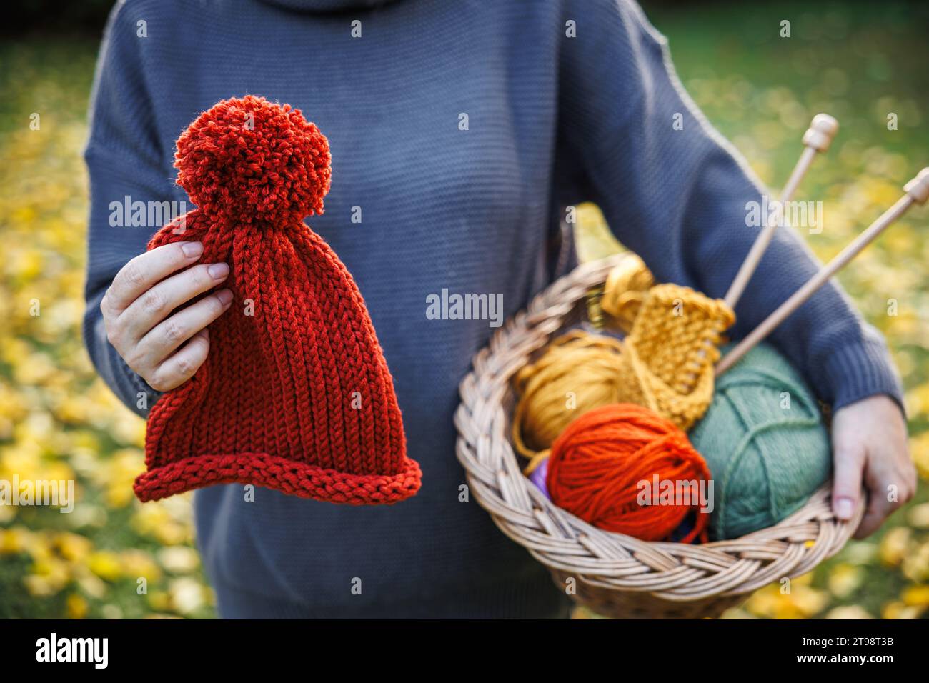 Maglia e uncinetto. Donna con cappello in maglia rossa fatto a mano e palle di lana nel cesto Foto Stock
