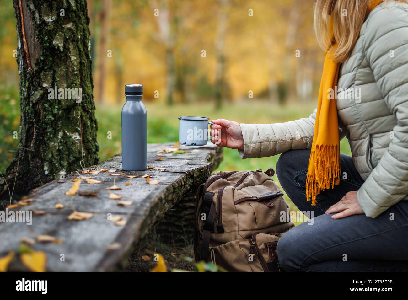 Donna che riposa durante le escursioni nella foresta autunnale. Escursionista che beve una bevanda calda dalla tazza da viaggio. Rinfresco all'aperto Foto Stock