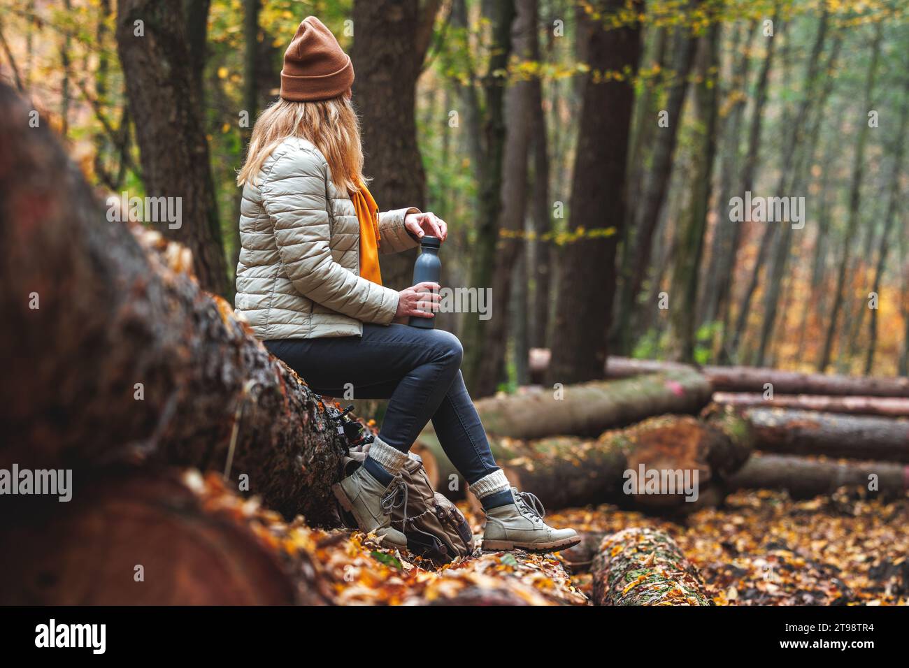 Ristoro durante le escursioni nella natura. Donna con thermos che riposa sul tronco nella foresta autunnale Foto Stock