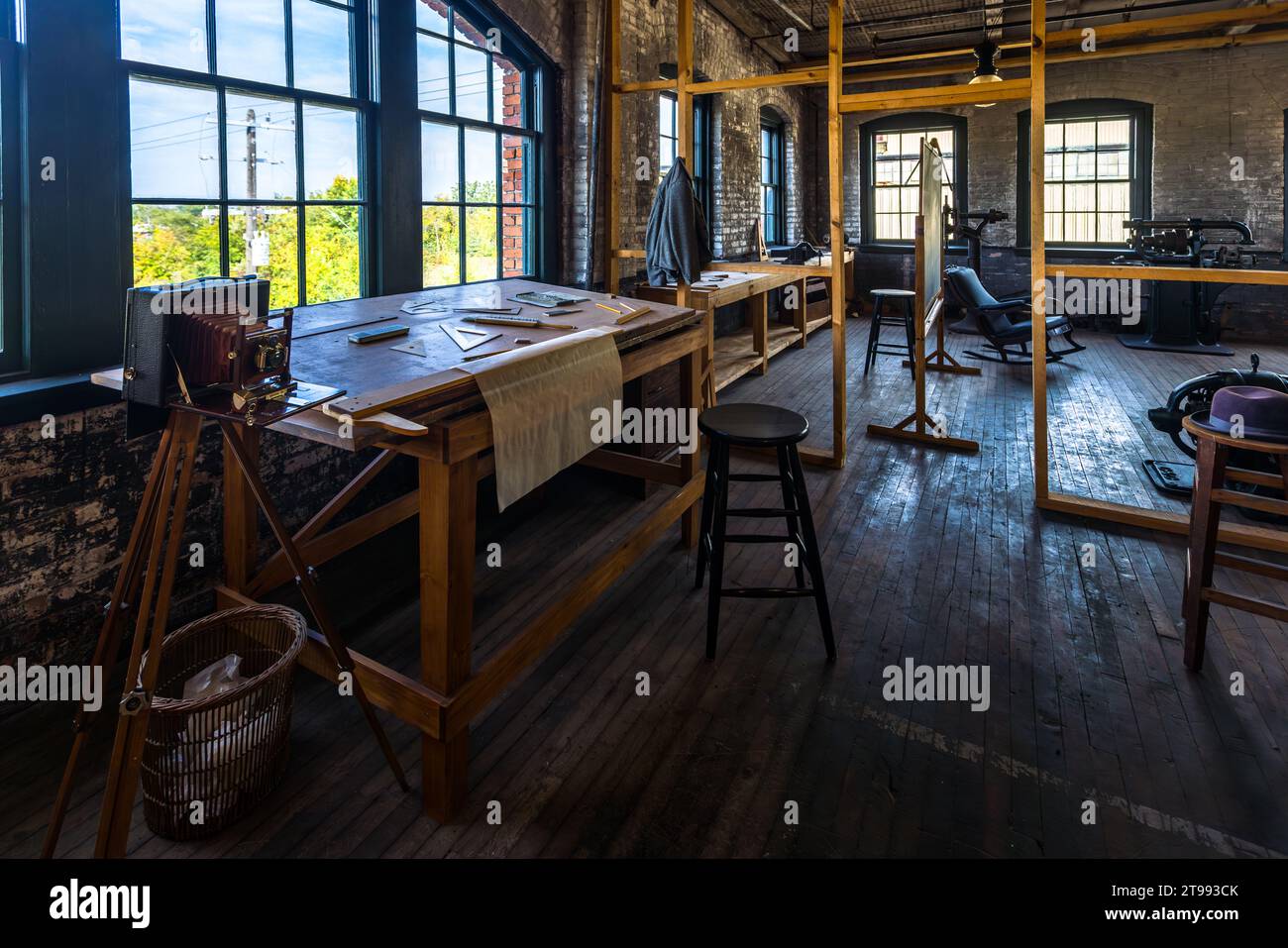 Una macchina fotografica a lastra storica su un treppiede di legno si trova accanto a tavoli da disegno nella sala sperimentale ricostruita del Ford Piquette Plant a Detroit, Michigan, Stati Uniti. In questa stanza del terzo piano strettamente sorvegliata, Henry Ford e un piccolo team di fiducia hanno sviluppato la Ford Model T per circa un anno, a partire dal gennaio 1907. Costruito nel 1904, il Ford Piquette Plant è considerato il più antico edificio sopravvissuto originariamente costruito per la produzione di automobili che rimane aperto al pubblico. Foto Stock