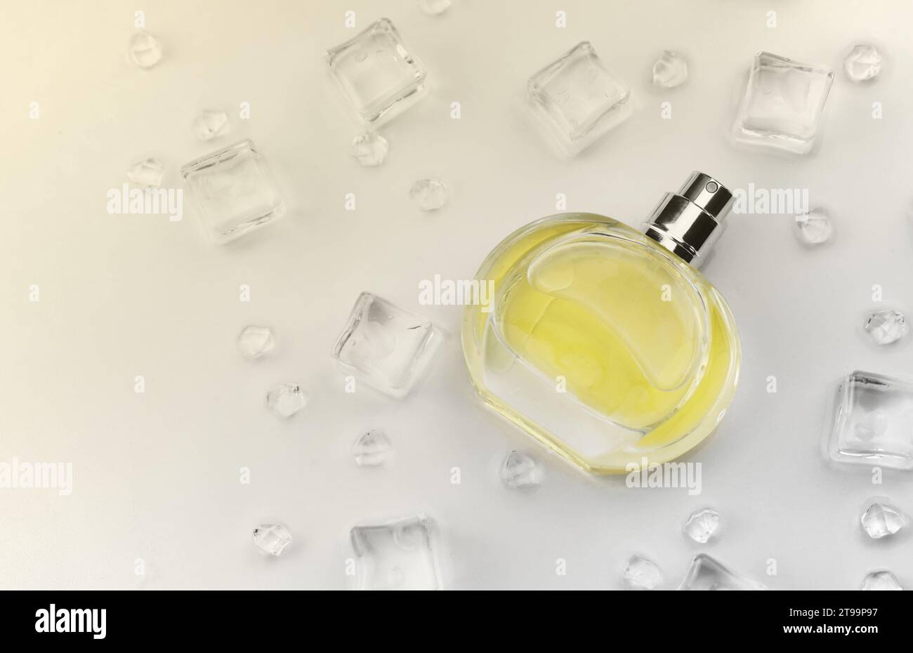 Bottiglia gialla di profumo femminile, fotografia oggettiva della bottiglia di profumo in cubetti di ghiaccio e acqua su tavolo bianco. Vista dall'alto. Foto del prodotto mockup, concetto di freschezza e aroma Foto Stock