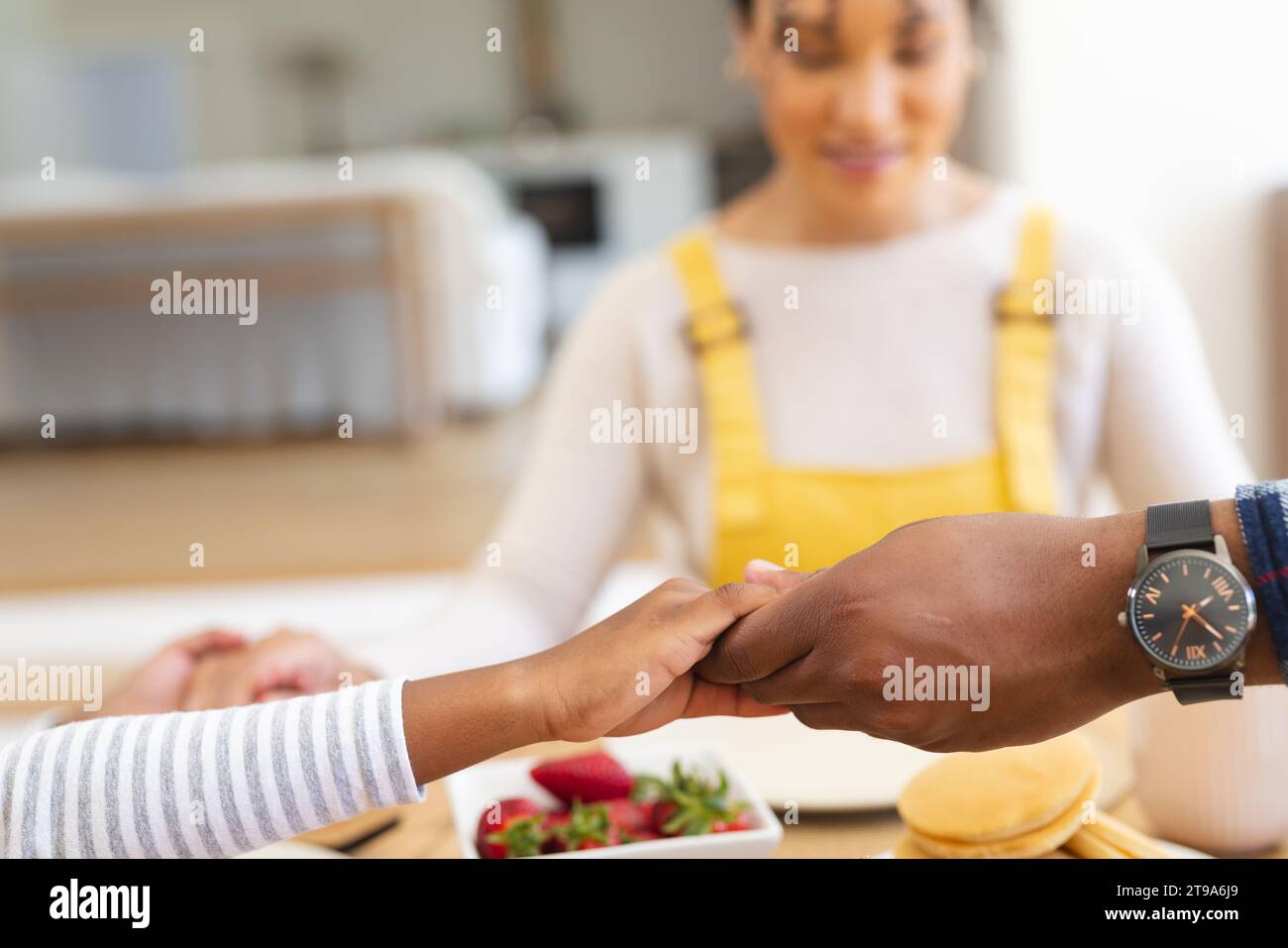 Famiglia afro-americana che si tiene per mano e prega al tavolo nella sala da pranzo a casa, spazio fotocopie. Insieme, genitorialità, infanzia, religione, cibo e.. Foto Stock
