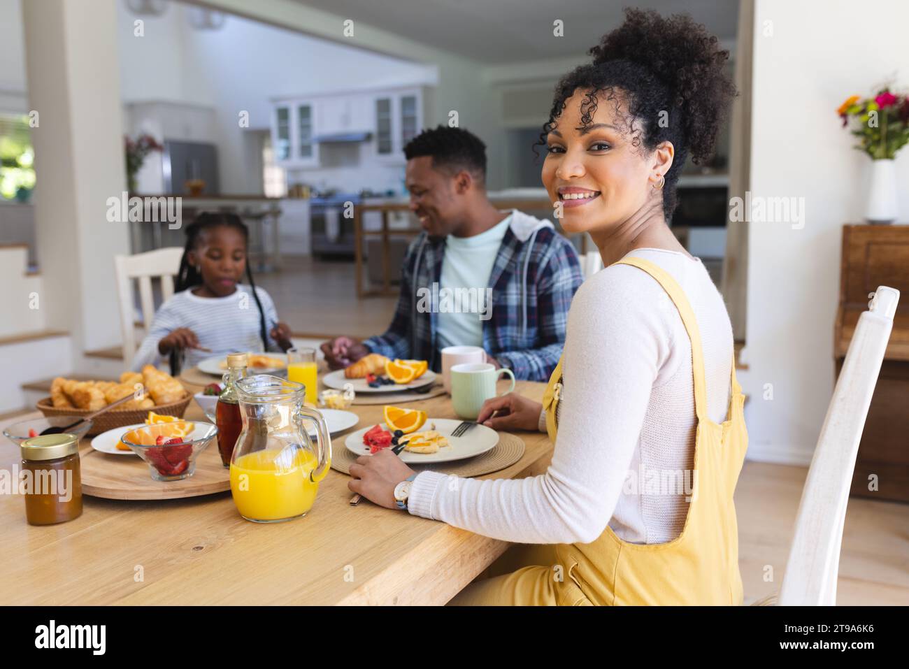 Felice donna afro-americana seduta al tavolo, con uno spuntino con la famiglia a casa, spazio fotocopie. Insieme, genitorialità, infanzia, cibo e bevande, fare Foto Stock