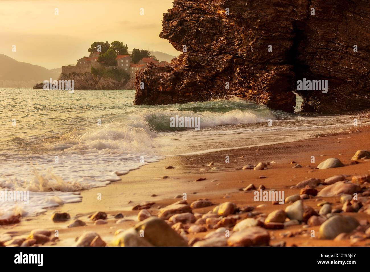 Case sull'isola di Sveti Stefan al tramonto, vicino a Budva, Montenegro, vista dall'angolo basso dalla spiaggia di Crvena Glavica Foto Stock