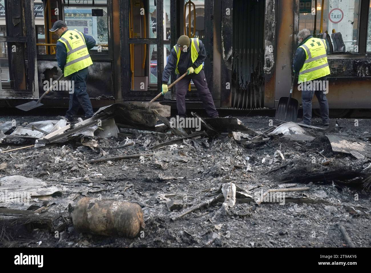 I detriti vengono eliminati da un Luas e un autobus bruciati in o'Connell Street a Dublino, in seguito a scene violente nel centro della città il giovedì sera. I disordini si verificarono dopo un attacco a Parnell Square East, dove cinque persone rimasero ferite, tra cui tre bambini piccoli. Data immagine: Venerdì 24 novembre 2023. Foto Stock