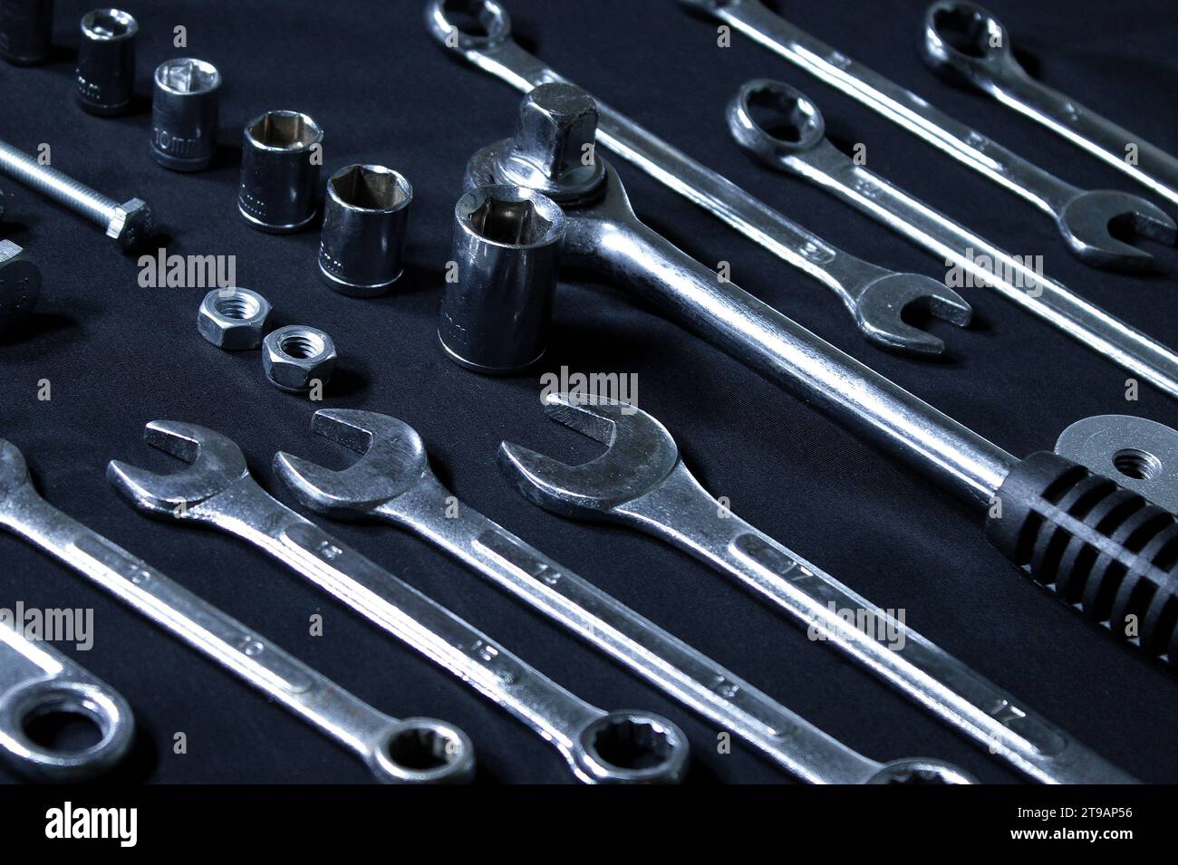 Set lucido in acciaio di chiavi, bussole, cricco a sgancio rapido e componenti hardware disposti in ordine sulla superficie nera Foto Stock