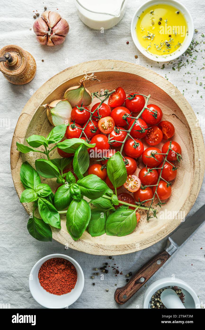 Piatti classici italiani: Pomodori e basilico fresco su un piatto di legno con altri ingredienti, olio d'oliva e aglio, vista dall'alto Foto Stock