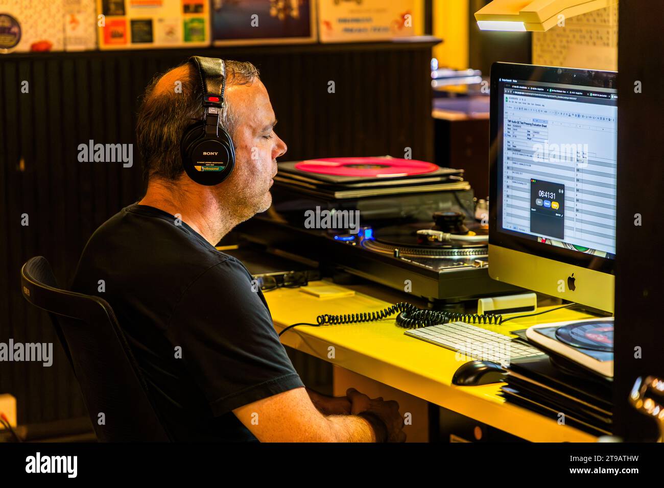 Un ingegnere del suono con le cuffie indossa ispeziona un vinile rosso appena stampato su un giradischi a una scrivania di controllo qualità presso Third Man Pressing a Detroit, Michigan, Stati Uniti, registrando il risultato su un computer vicino. I primi dischi di ogni nuova matrice di stampa devono superare questo controllo audio da parte di un ascoltatore addestrato prima che lo stabilimento di stampa dell'etichetta indipendente Third Man Records (Jack White, Ben Blackwell, Ben Swank) rilasci l'edizione. Foto Stock