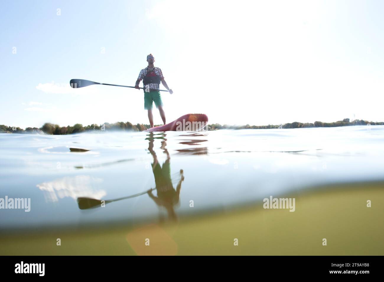 Immagine a livello diviso di un uomo in piedi su paddleboard (SUP) contro un cielo esploso. Foto Stock