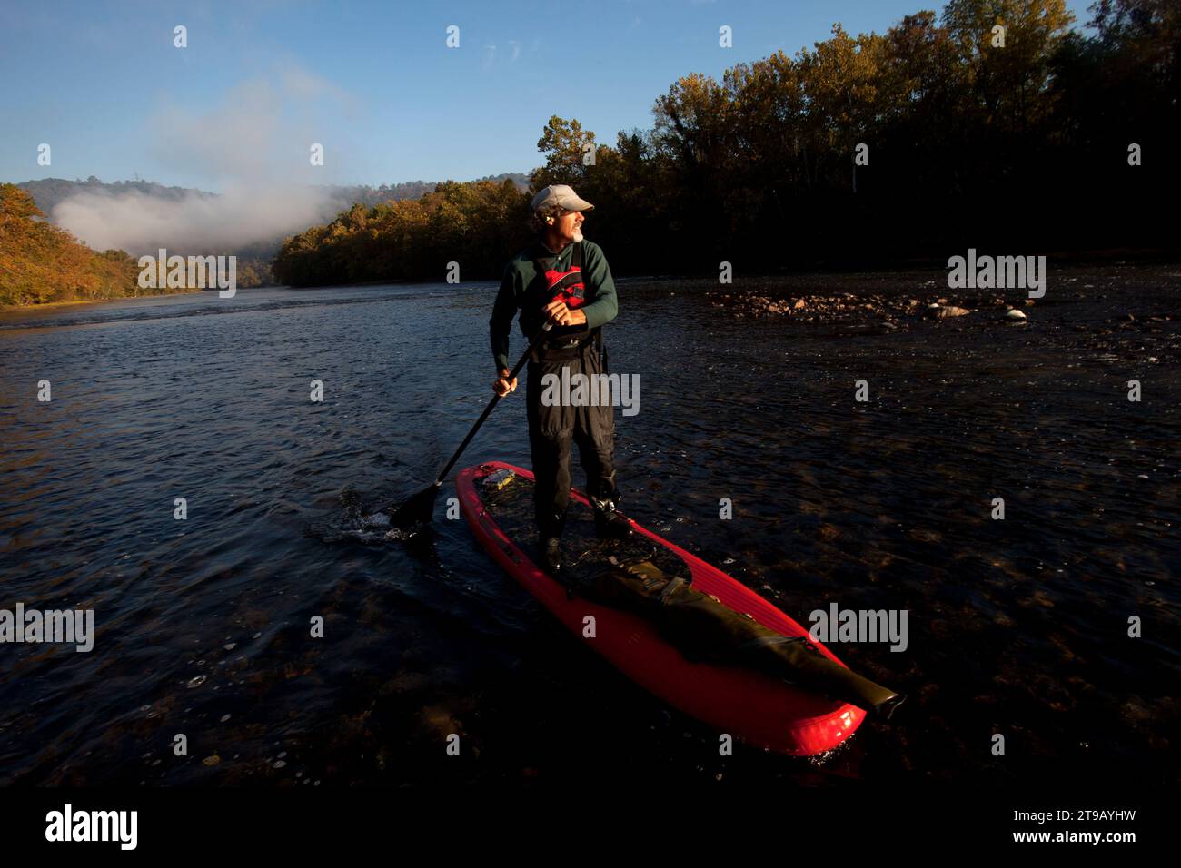 Un uomo/cacciatore su una tavola da paddle con un fucile alla luce del mattino. Foto Stock