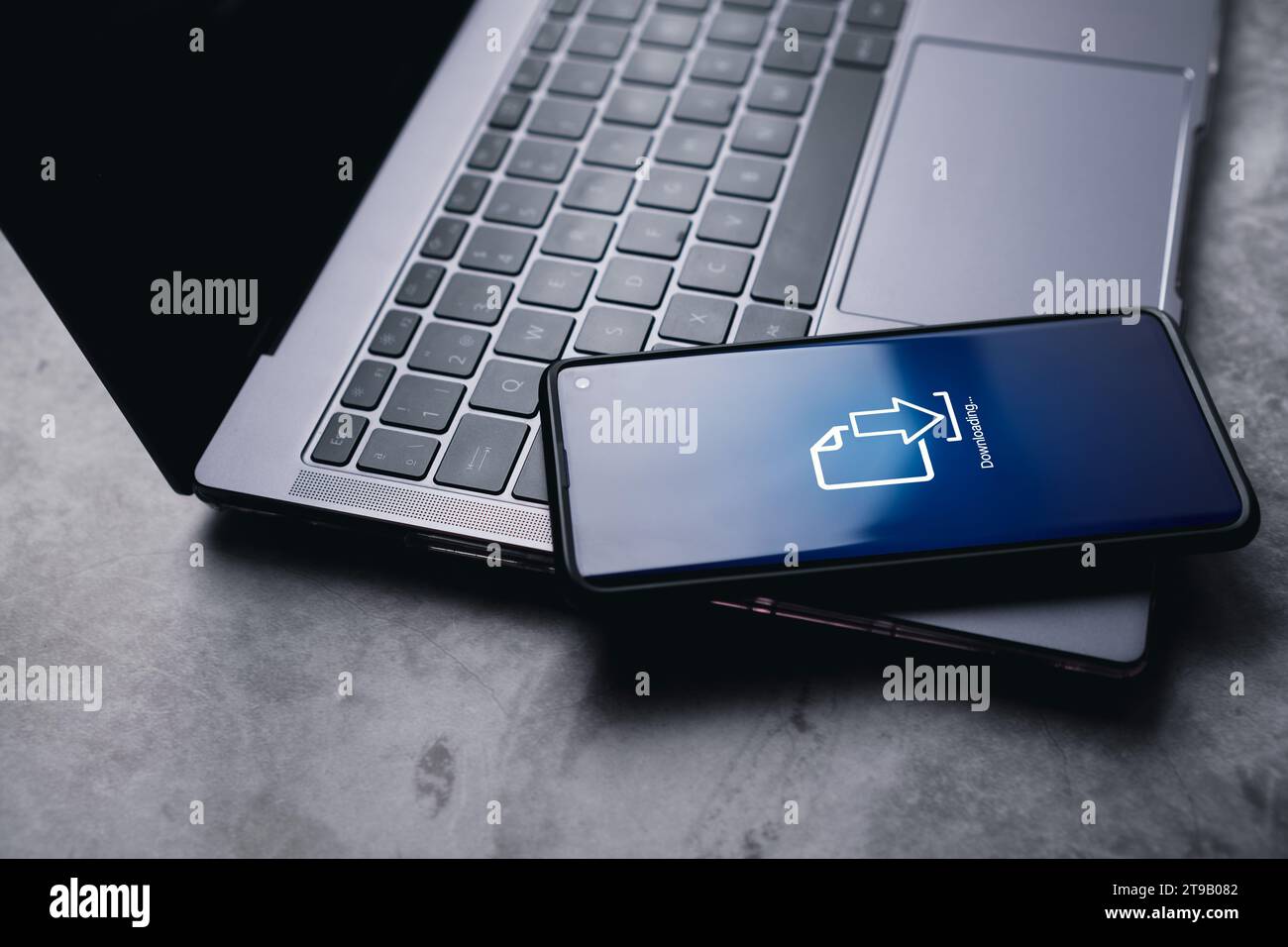 Smartphone posizionato sul computer portatile durante il download di file o l'installazione di software sul telefono. Backup dei dati. Archiviazione cloud. Sicurezza informatica. Foto Stock