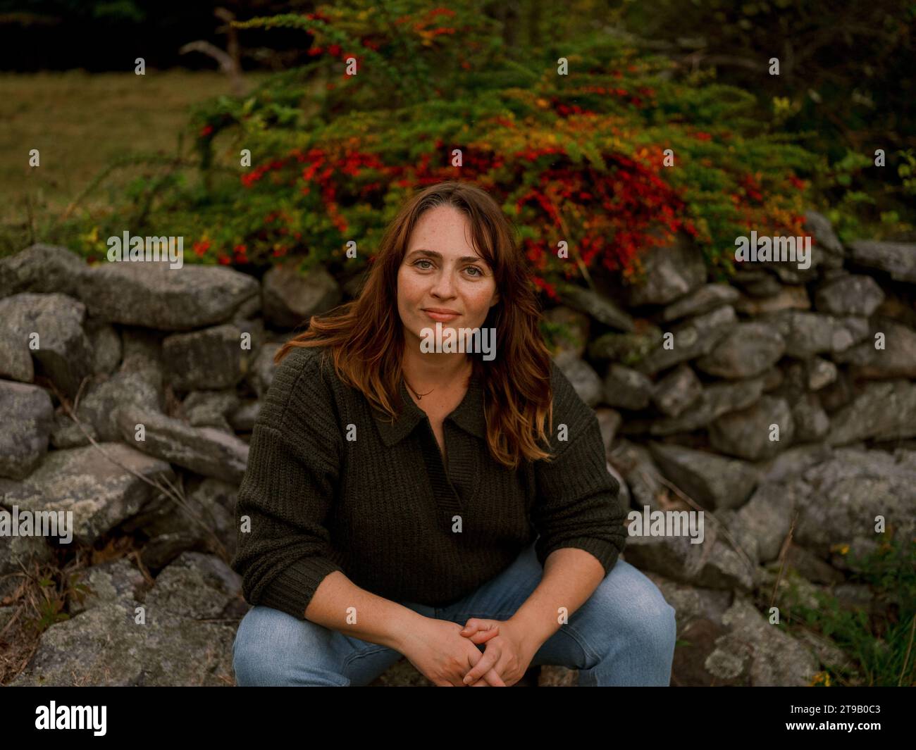 Donna seduta nella foresta, espressione gentile, di fronte alla telecamera tra Re Foto Stock
