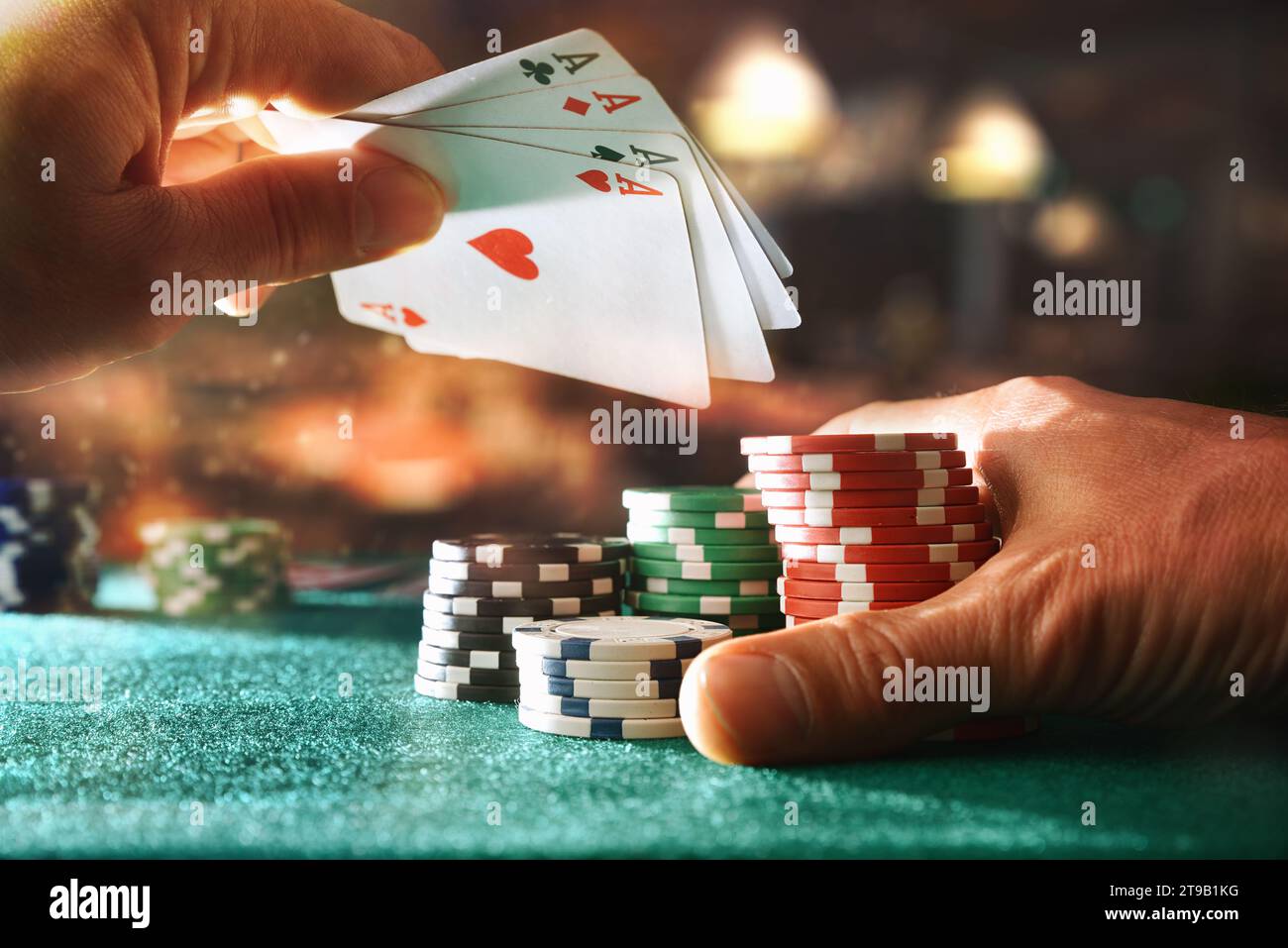 Mano con un set di assi e chip di scommessa su un tappetino da gioco verde sul tavolo della sala giochi. Vista frontale. Foto Stock