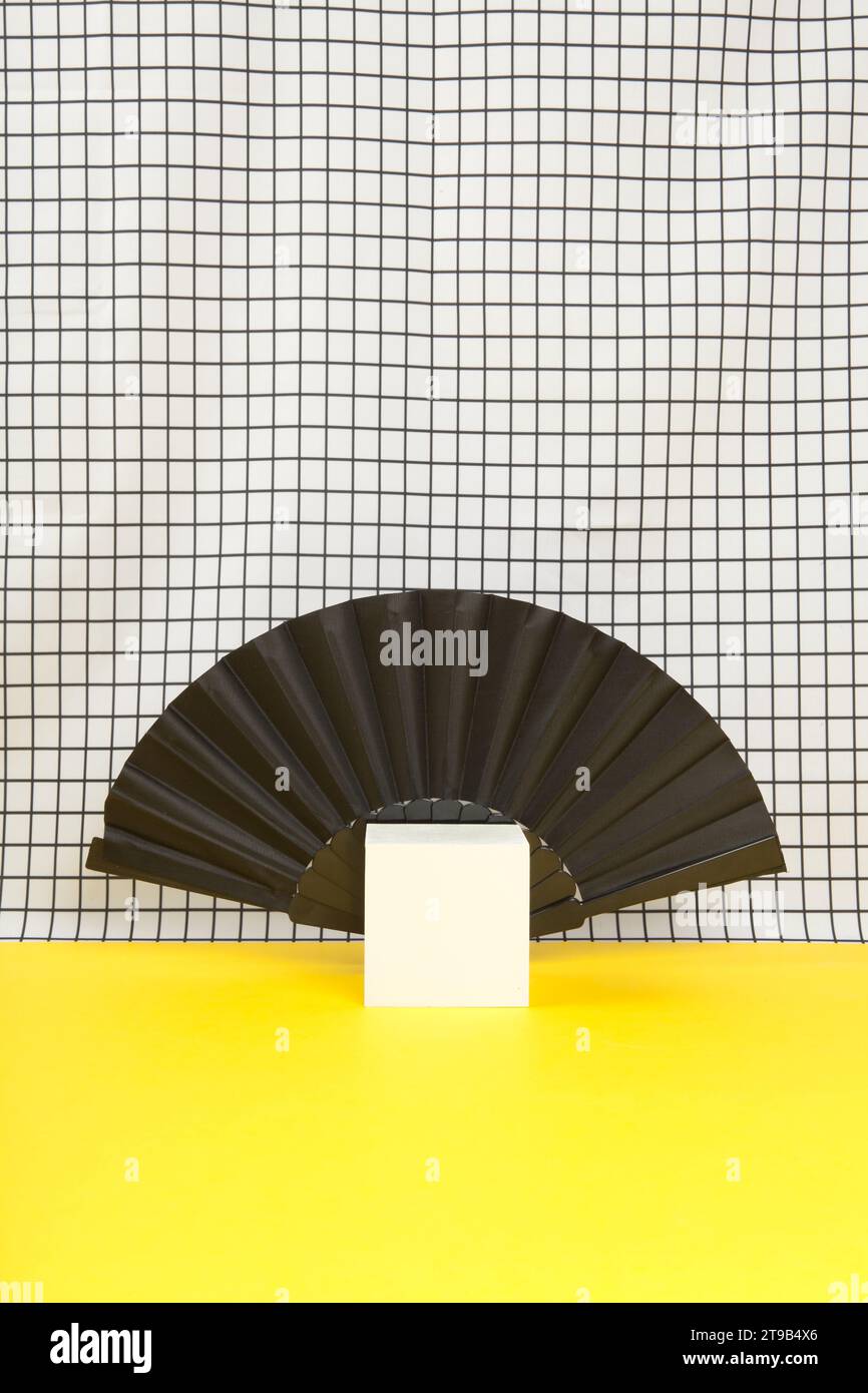 un ventilatore posizionato dietro un cubo bianco come metafora per il collare di un vampiro su uno sfondo a griglia bianco e nero e pavimento giallo. oggetto vuoto di Foto Stock