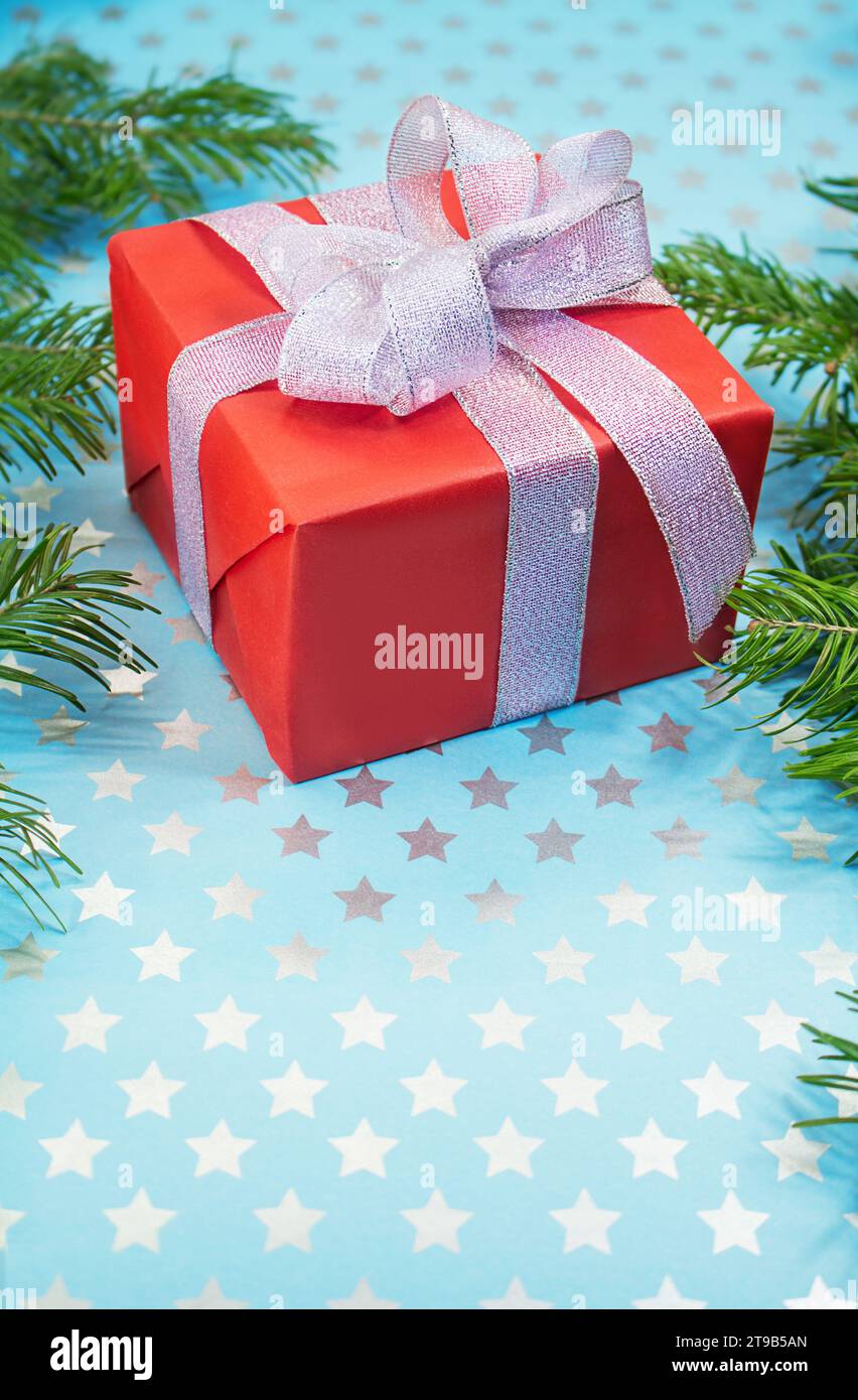 Confezione regalo rossa con fiocco in argento lucido su sfondo blu con stelle e rami di abete. Natale, Capodanno, San Valentino, compleanno, festa. Verticale. Foto Stock