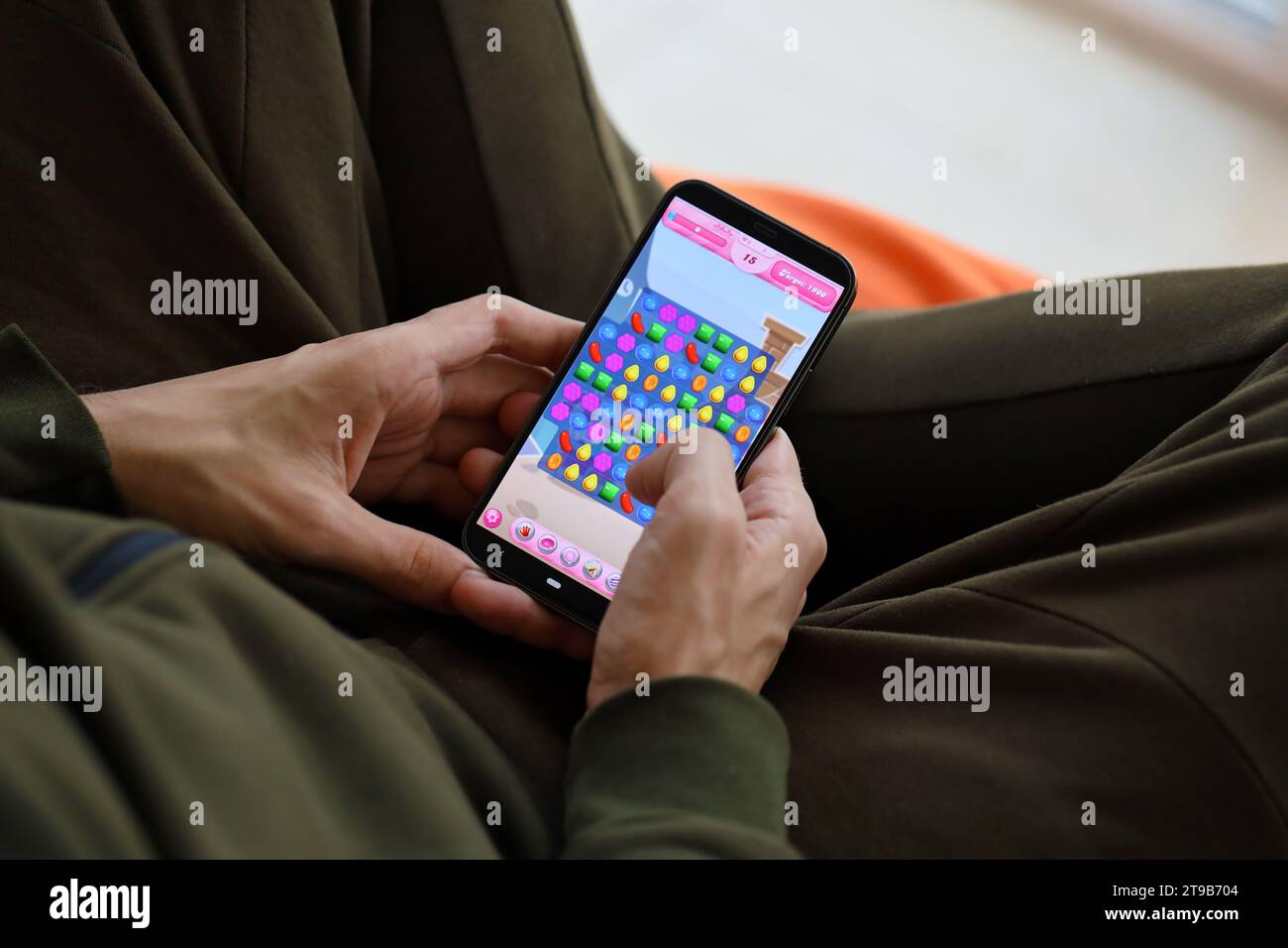 Candy Crush Saga gioco per dispositivi mobili iOS su schermo dello smartphone iPhone 15 in mani maschili durante l'azione di gioco mobile. Gioco e intrattenimento mobile su devi portatile Foto Stock