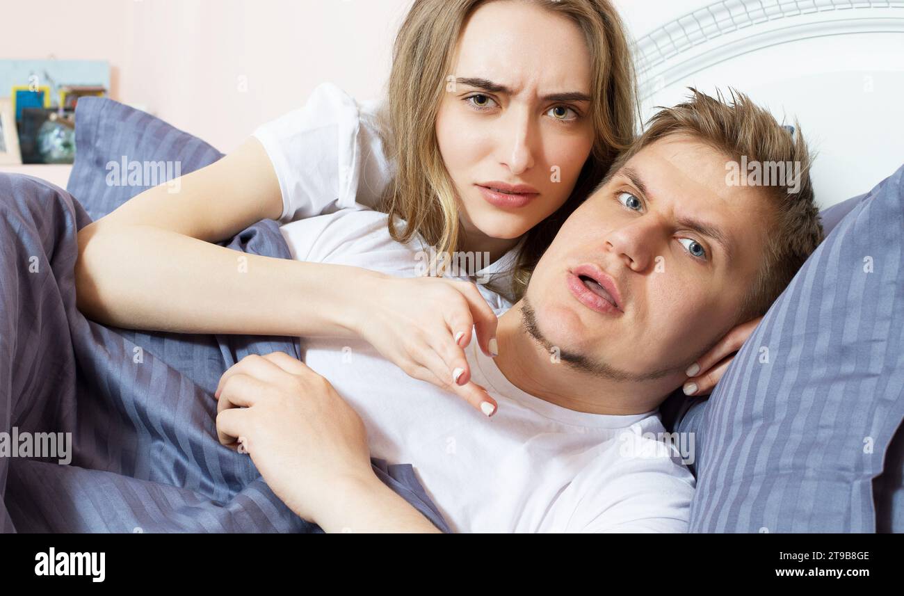 La coppia scontenta è sdraiata a letto e guarda la telecamera, problemi nelle relazioni, persone arrabbiate, cattivo sonno Foto Stock