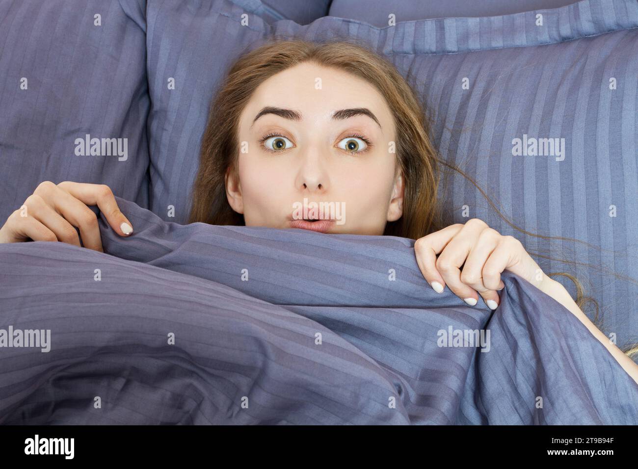 Bella donna sorpresa sdraiata nel letto dopo aver dormito. Ragazza adolescente con gli occhi aperti con coperta grigia. Concetto mattutino. Vista dall'alto con plac Foto Stock