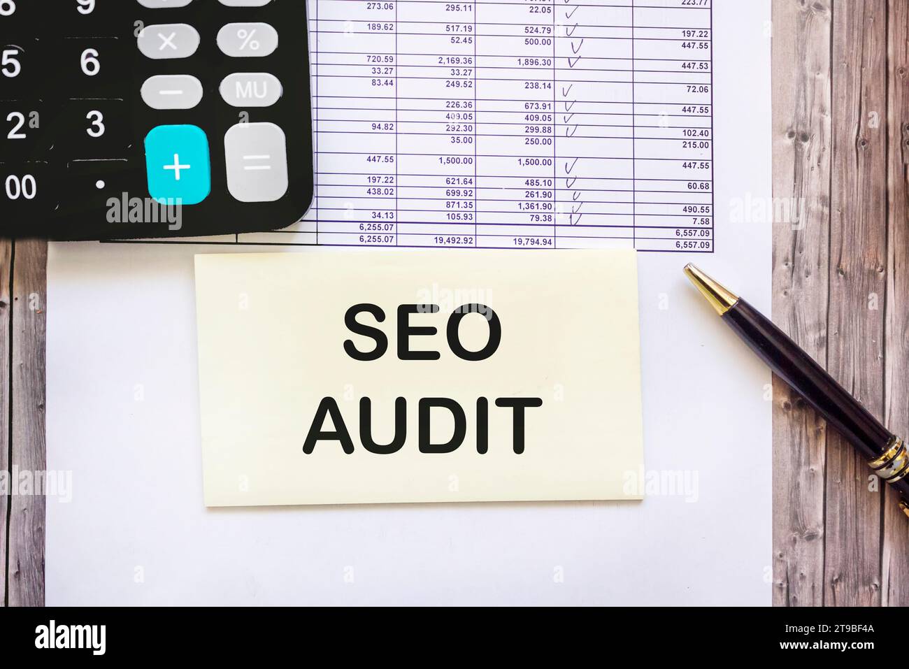 Su un tavolo di legno c'è una calcolatrice nera, una penna e un blocco note con l'iscrizione SEO AUDIT. Concetto aziendale. Foto Stock