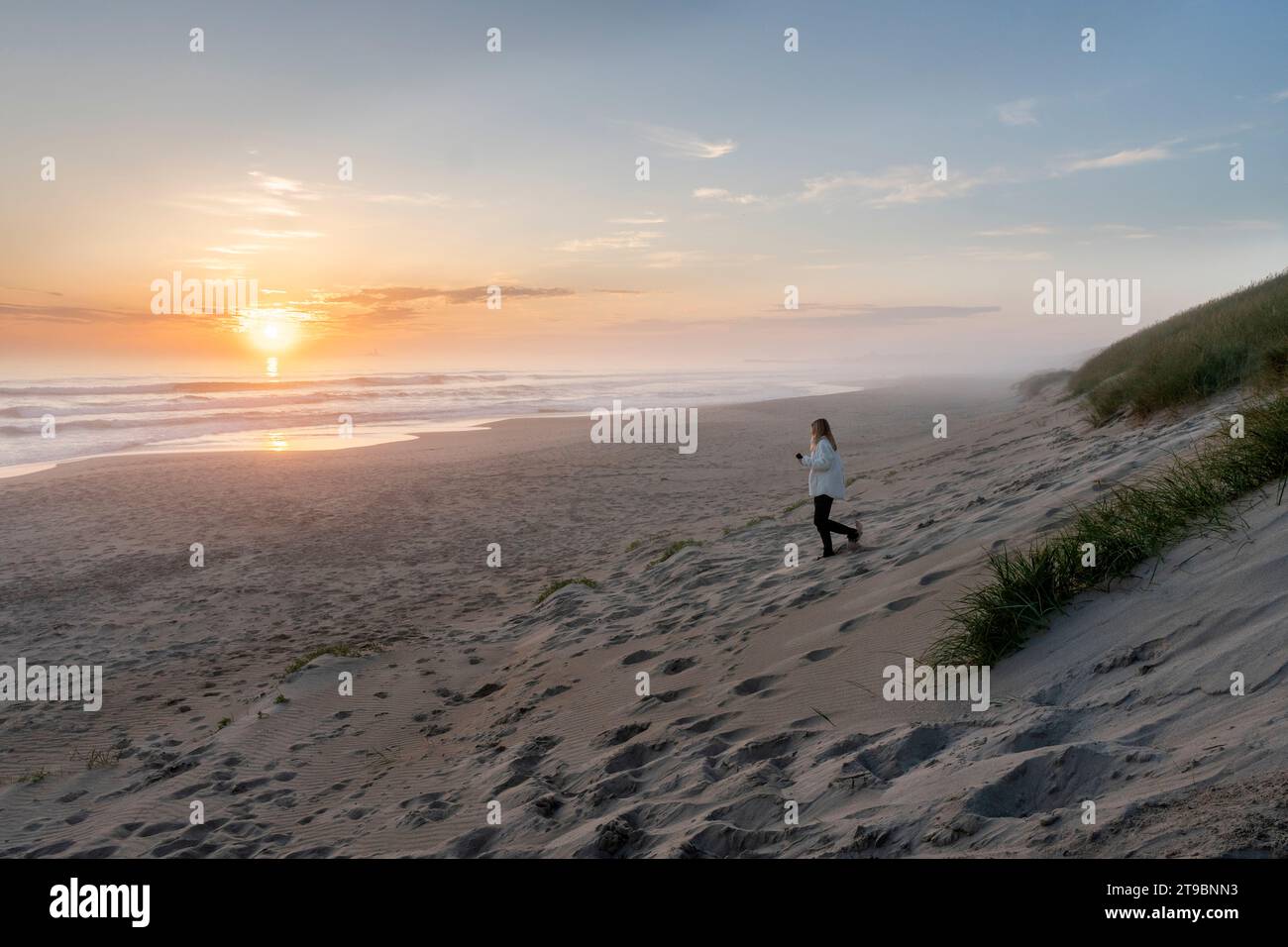 Donna che cammina su una spiaggia vuota al tramonto Foto Stock