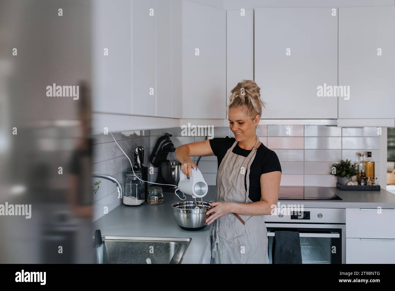 Giovane donna che usa il mixer in cucina Foto Stock