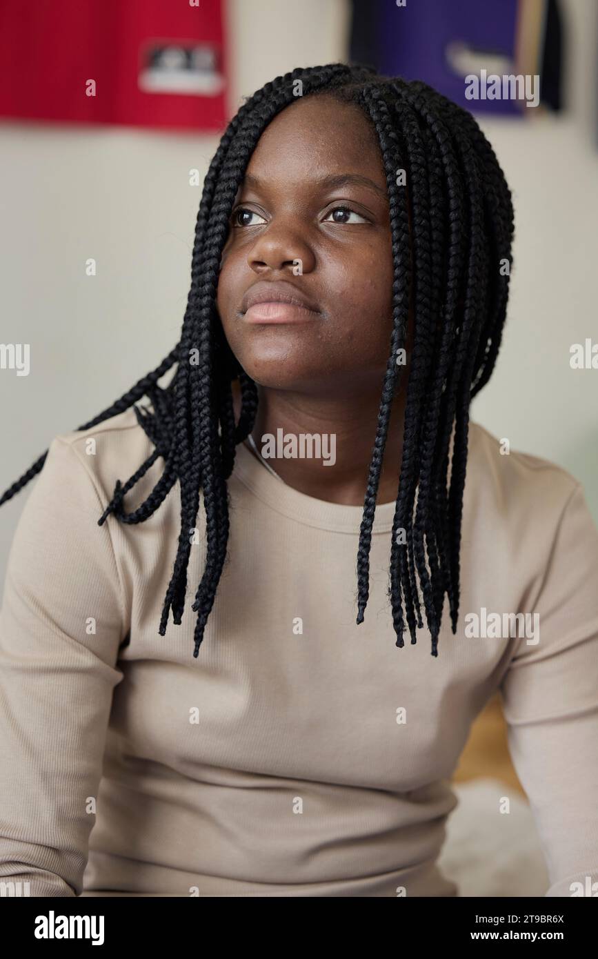 Adolescente contemplativa con capelli intrecciati seduta a casa Foto Stock