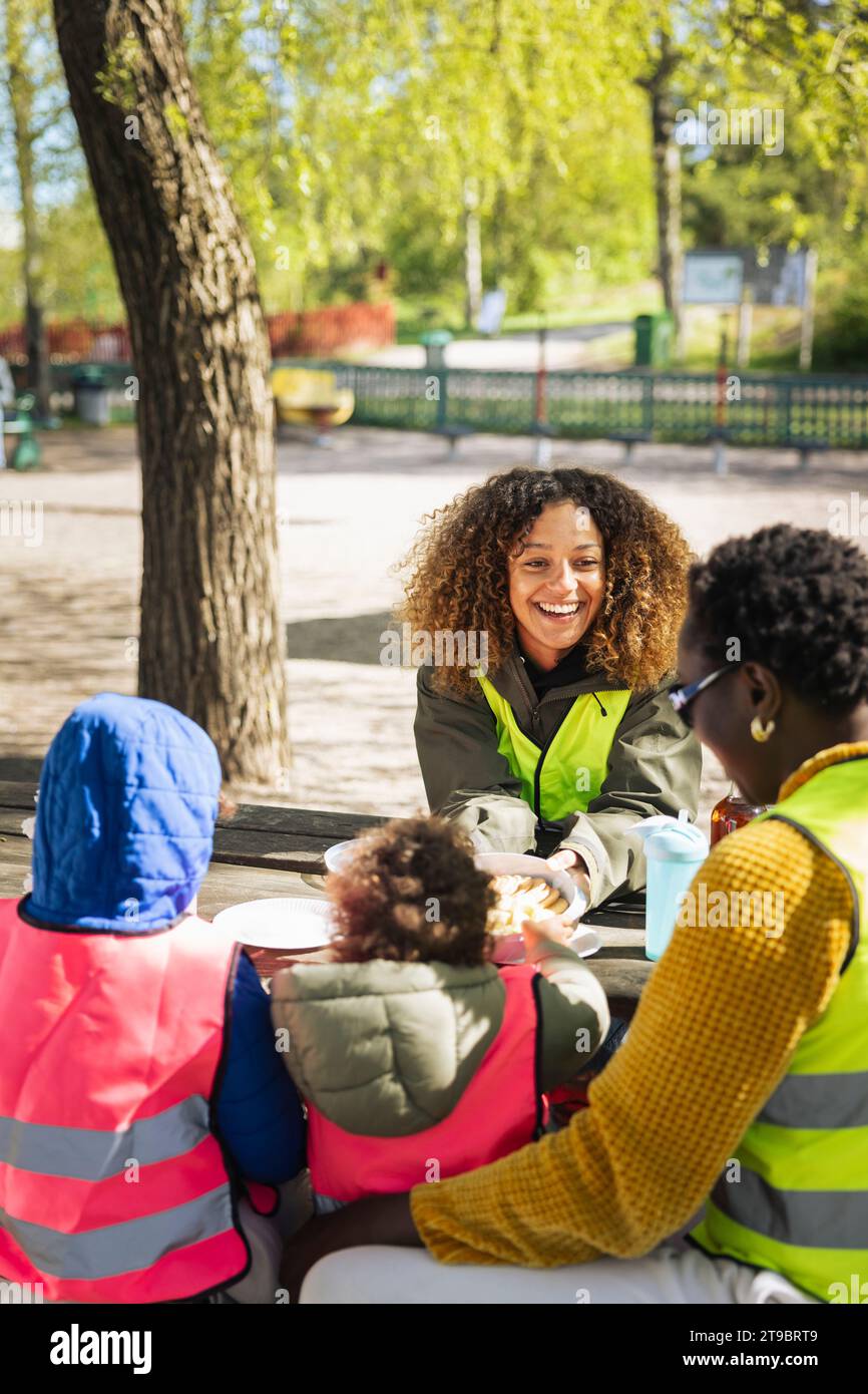 Donna sorridente che parla con un'amica seduta accanto ai bambini a tavola Foto Stock