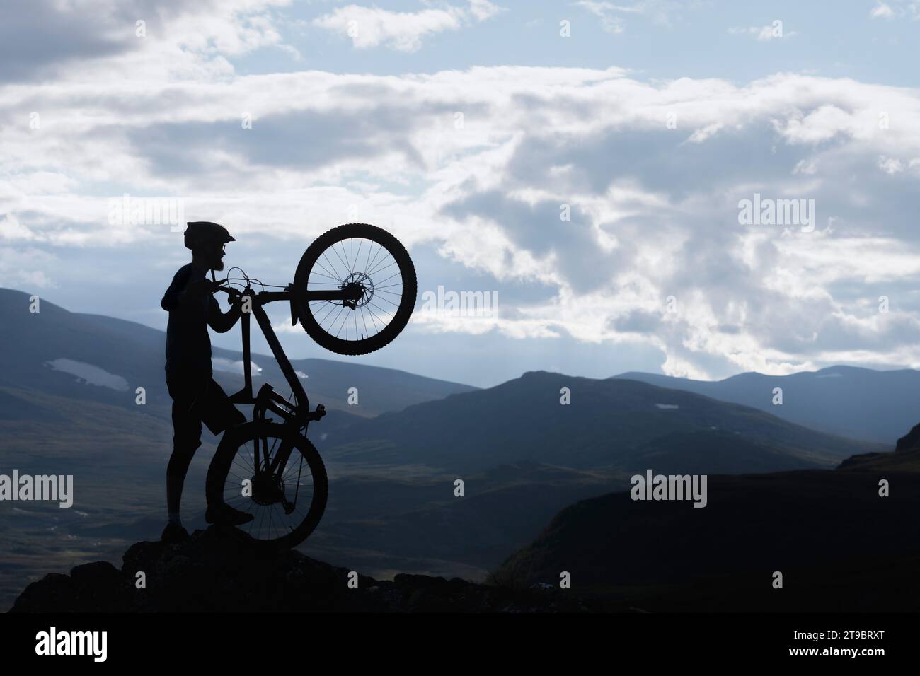 Silhouette ciclista in piedi con bicicletta sulla vetta della montagna contro il cielo Foto Stock
