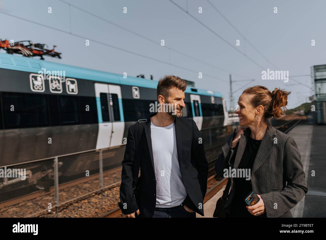 Felici pendolari uomini e donne che parlano mentre camminano alla stazione ferroviaria Foto Stock