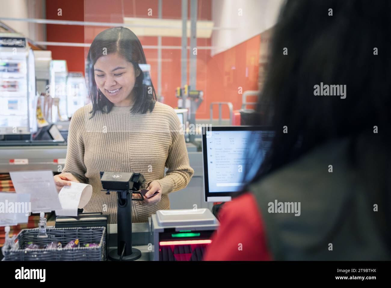 Una giovane cliente sorridente che riceve la ricevuta al momento del check-out nel supermercato Foto Stock
