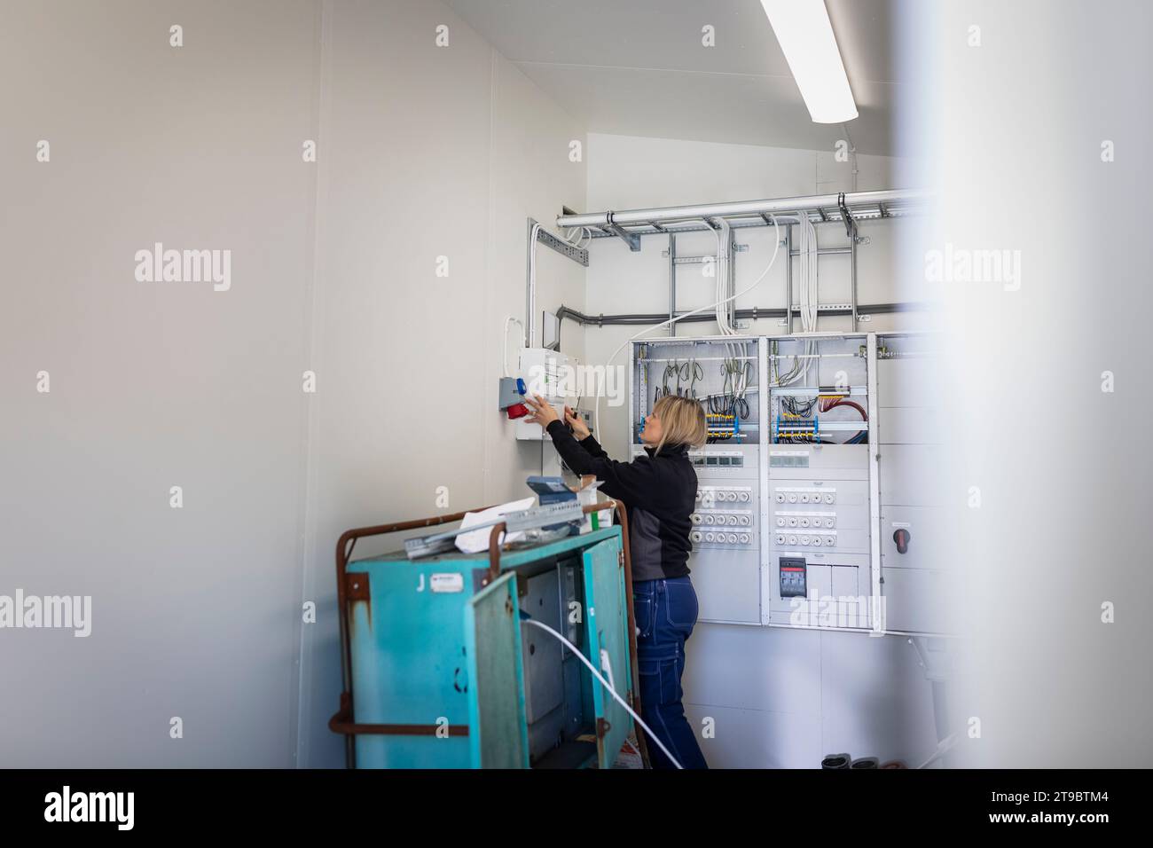 Elettricista femmina che installa la scatola fusibili mentre si trova in una sala metri presso l'industria Foto Stock