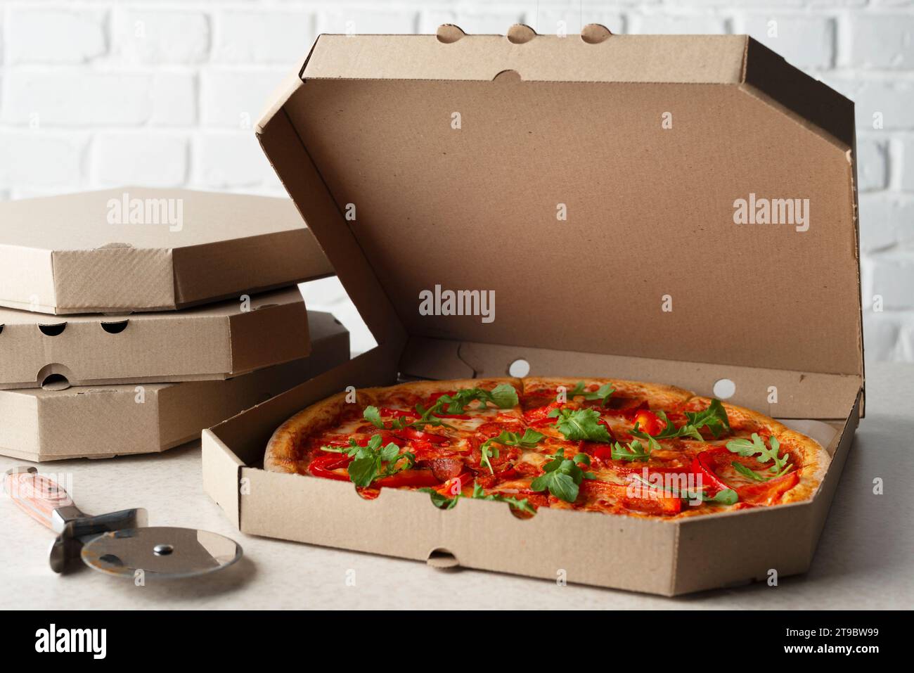 Grande pizza in scatola di cartone aperta e taglierina sul tavolo della cucina vista dall'alto Foto Stock