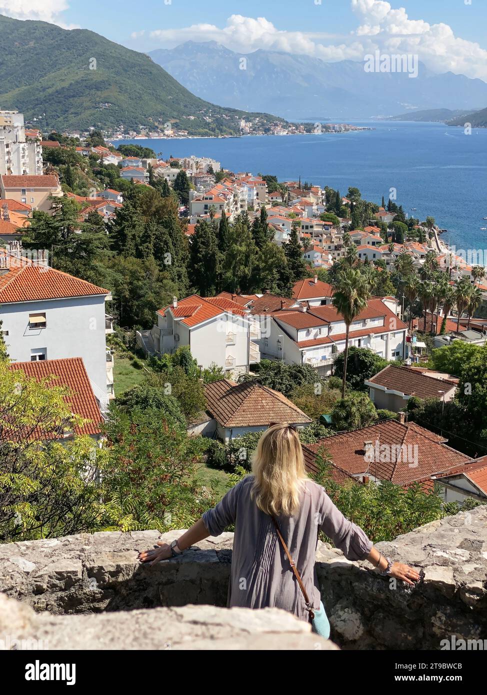Donna di mezza età che si rilassa alle mura della fortezza di Kanli Kula con vista su Herceg Novi e sulla baia di Cattaro Foto Stock