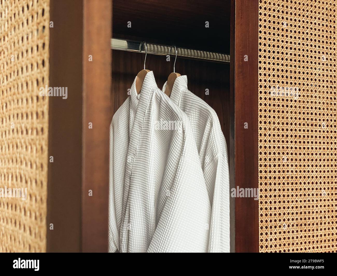 Due accappatoi bianchi e puliti appesi in un armadio di legno in un hotel di lusso o a casa. Concetto di relax e viaggio Foto Stock