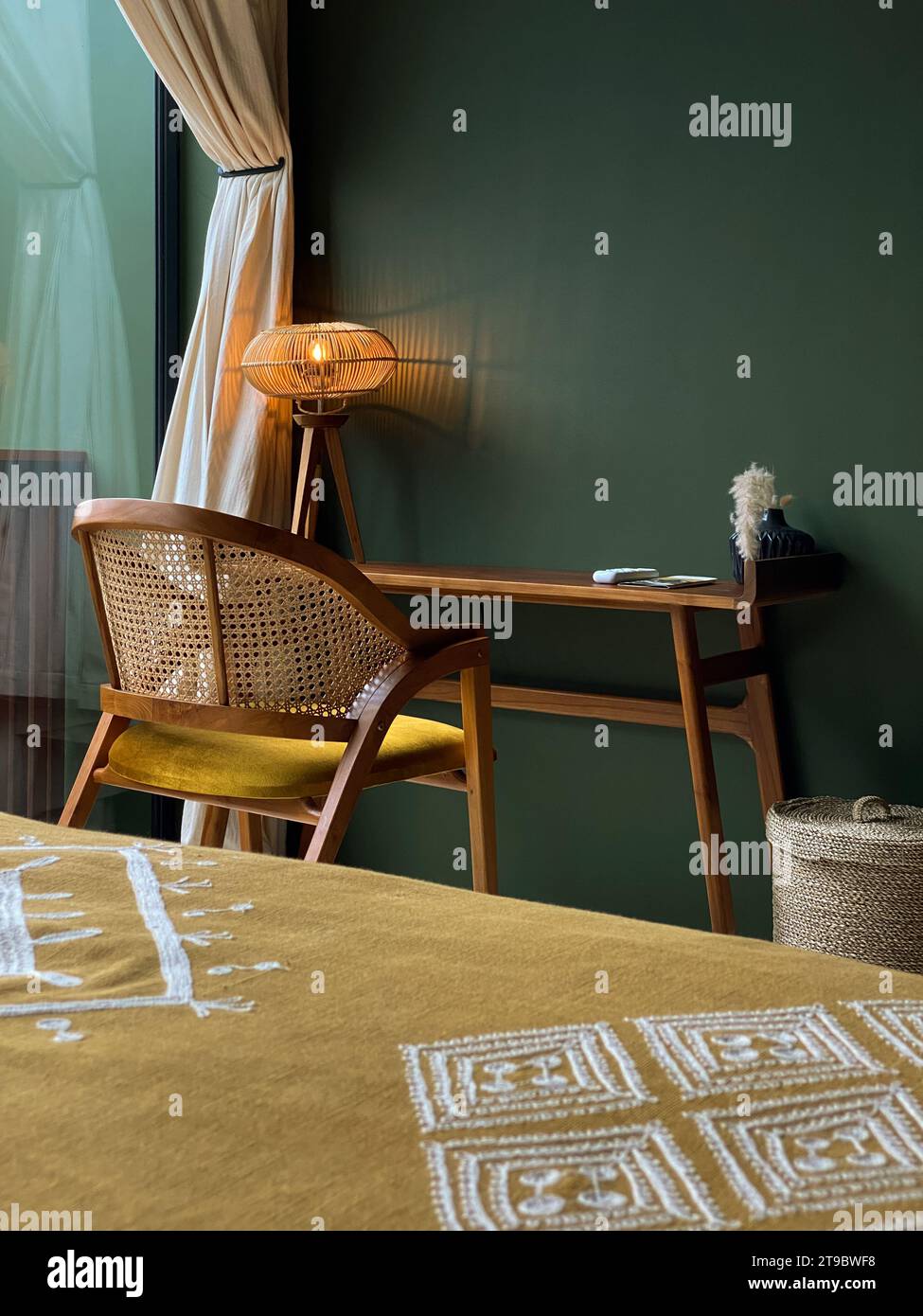 Area di lavoro con lampada da tavolo, tavolo in legno e sedia in rattan nella camera da letto Foto Stock